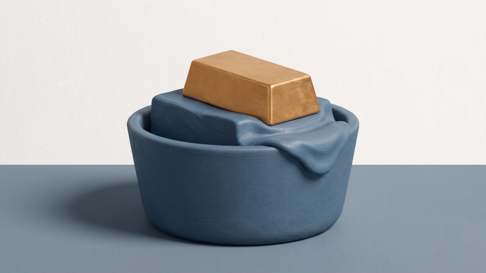 A smooth gold ingot rests on a block of matte blue clay that melts over the rim of a round blue basin. The objects sit on a grey surface against an off-white wall under soft light from the left.